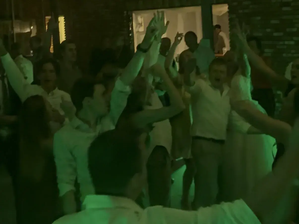 Handen in de lucht in groen licht op een volle dansvloer op een trouwfeest